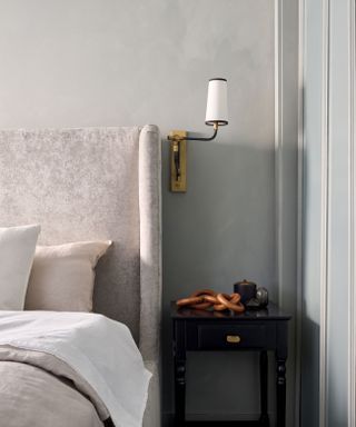 grey bedroom with high headboard and brass wall lamp