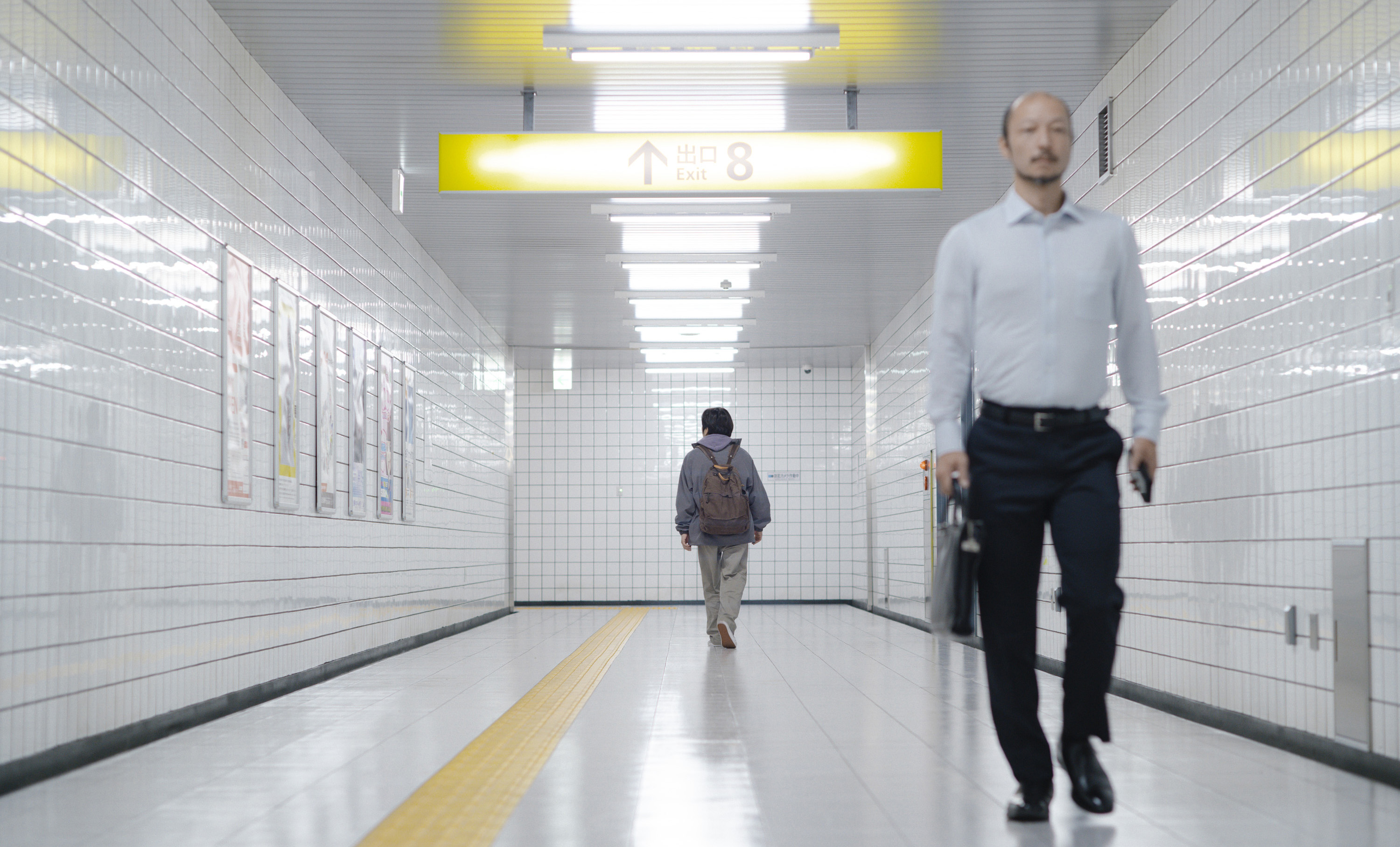 A man with a briefcase walking down a corridor with another man further away walking in the opposite direction