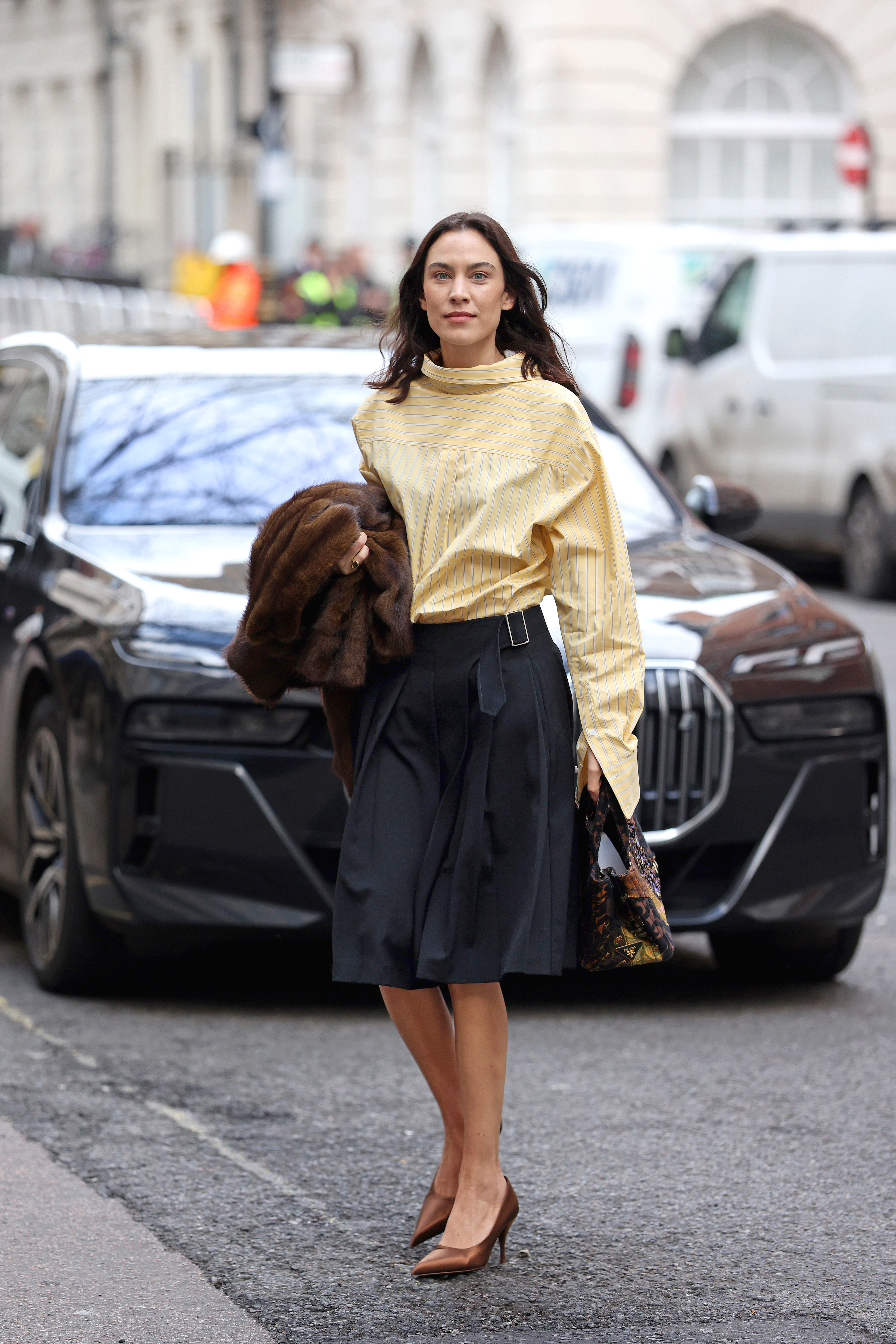 Alexa Chung wears a butter yellow skirt with a knee-length skirt and brown heels.