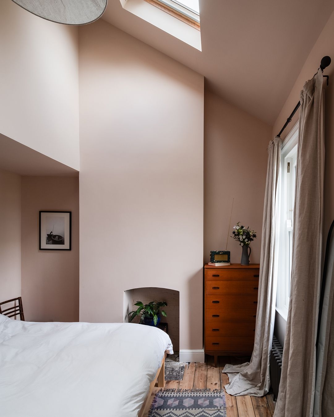 A bedroom painted in a pinky beige colour with natural wood floors. The ceilings are high and slightly pitched with glazing in the roof
