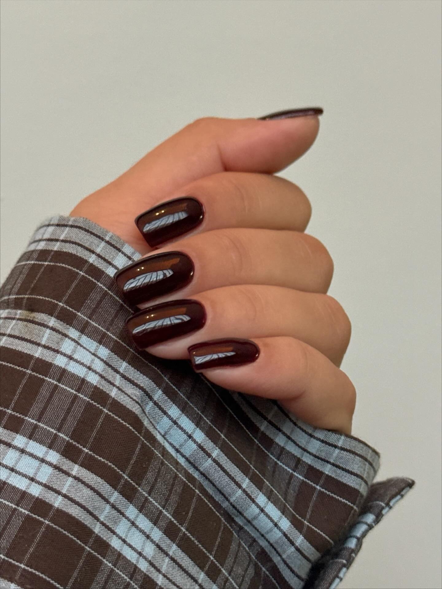 A woman wearing a blue and brown checked shirt with a glossy, ebony manicure