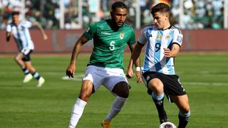 Julian Alvarez (R), in a blue and white striped shirt and black shorts, looks to keep the football from Adrián Jusino, wearing a green shirt and white shorts, during Argentina vs Bolivia. 