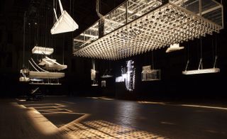 Large metal lighting structures hanging from the ceiling of an exhibition hall with wooden floor