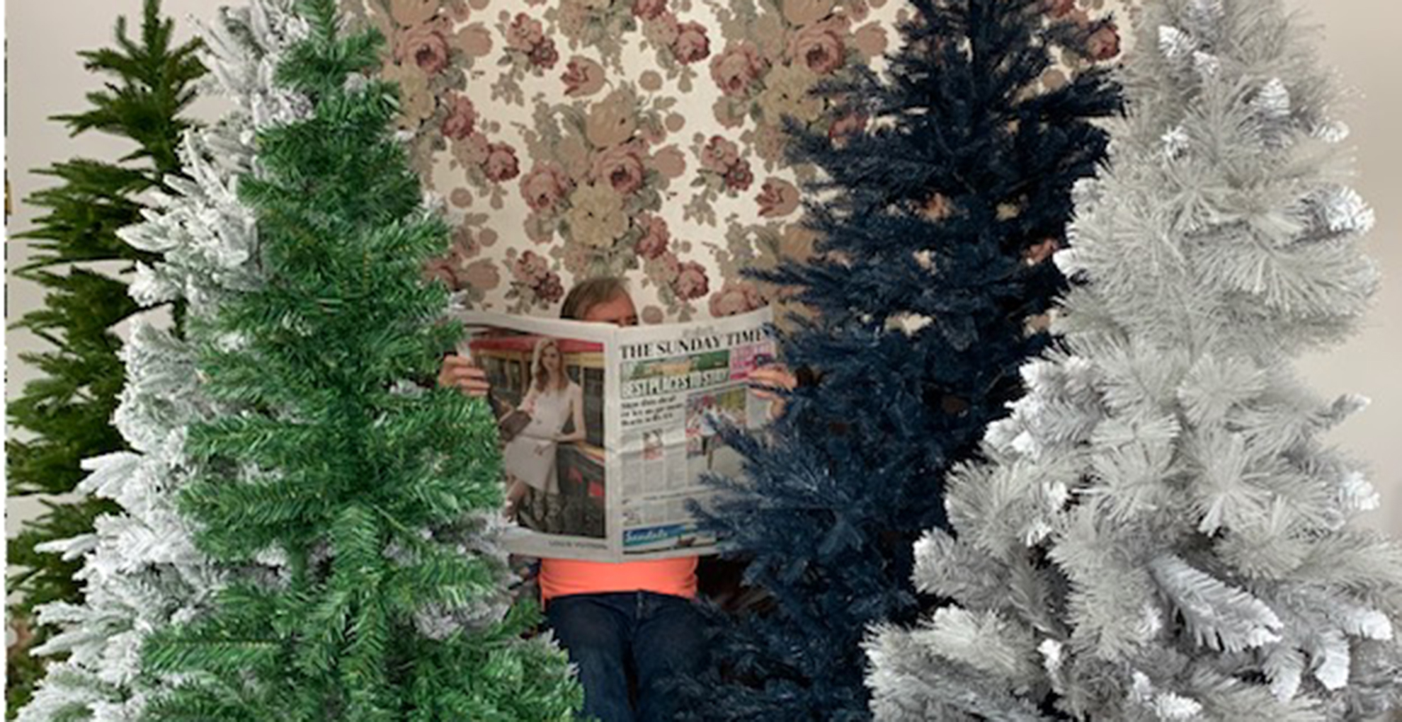 Many Christmas trees surrounding a man redaing the paper