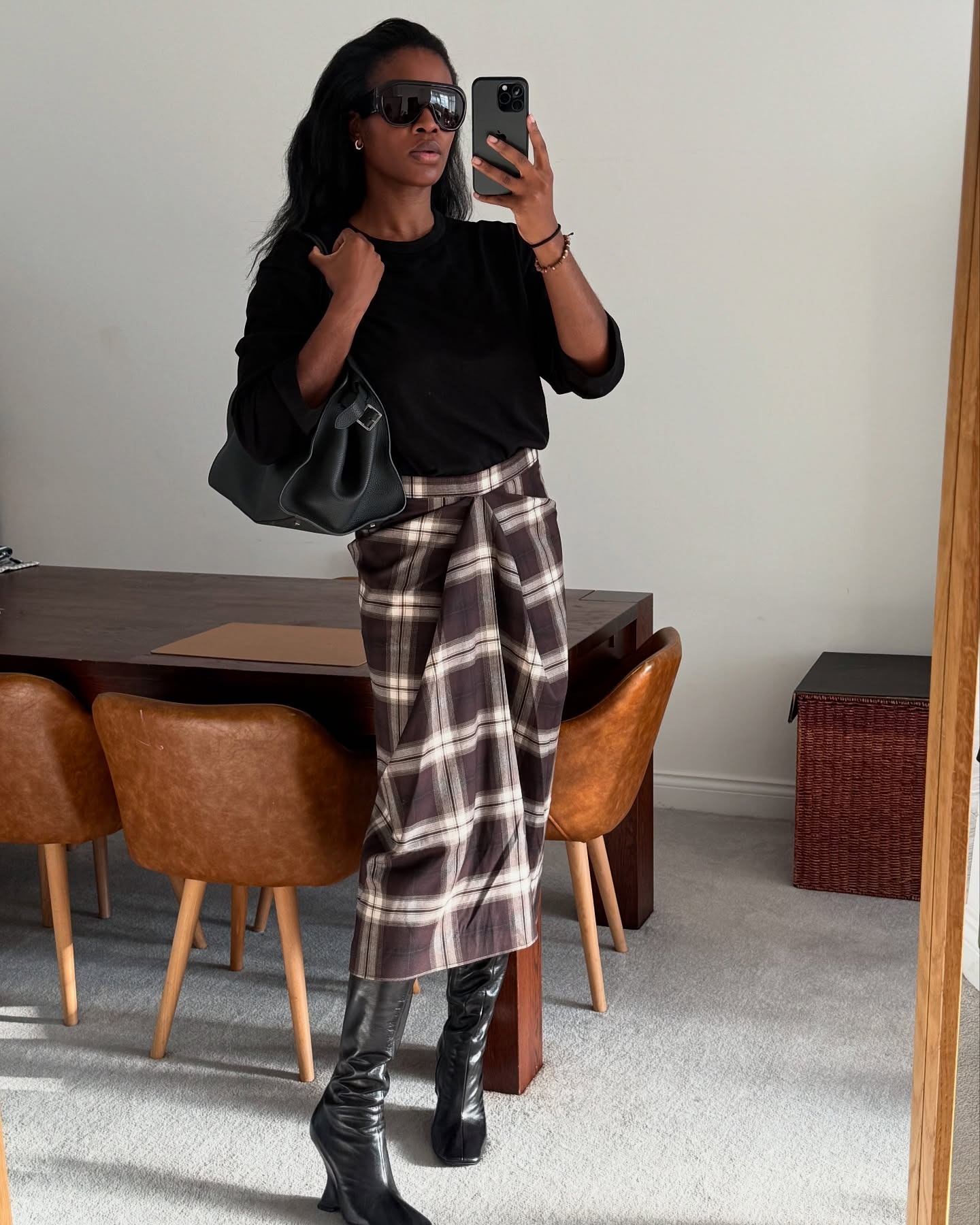 Influencer @nlmarilyn takes a mirror selfie wearing wedge boots and a checked skirt with a black jumper.