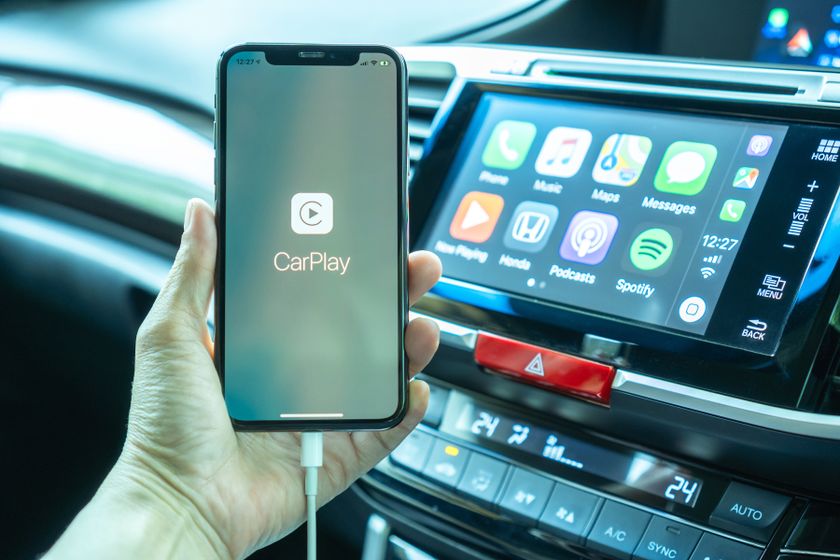 Photo d&#039;une personne tenant un téléphone à l&#039;intérieur d&#039;une voiture. L&#039;écran du téléphone affiche le logo CarPlay.