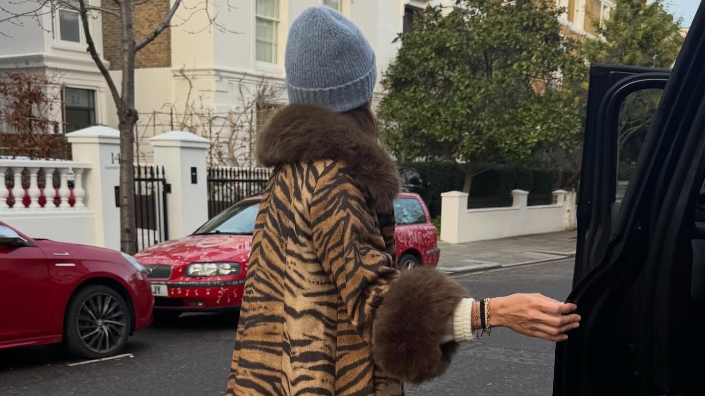 Woman wears a fur lined leopard print coat, blue beanie, light wash jeans and blue Vans slip ons. 