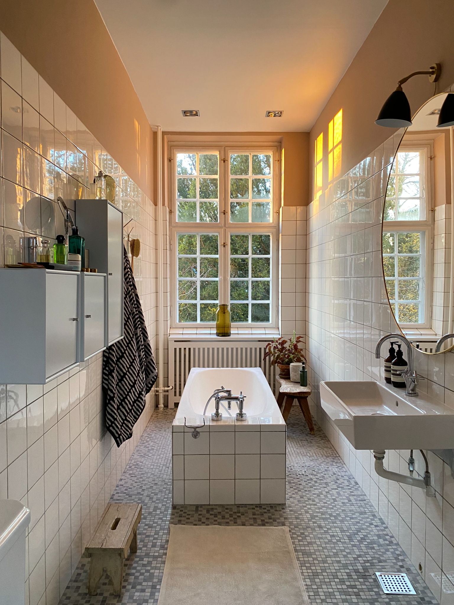 A Scandinavian style bathroom with white square tiles, a bath in the center of the room, and minimalist blue cabinets on the wall