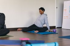 A woman performs a 90/90 hip mobility exercise, with both knees bent at 90&deg;, her left knee in front and her right knee out to the right side.