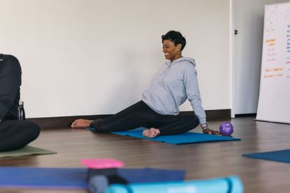 A woman performs a 90/90 hip mobility exercise, with both knees bent at 90&deg;, her left knee in front and her right knee out to the right side.
