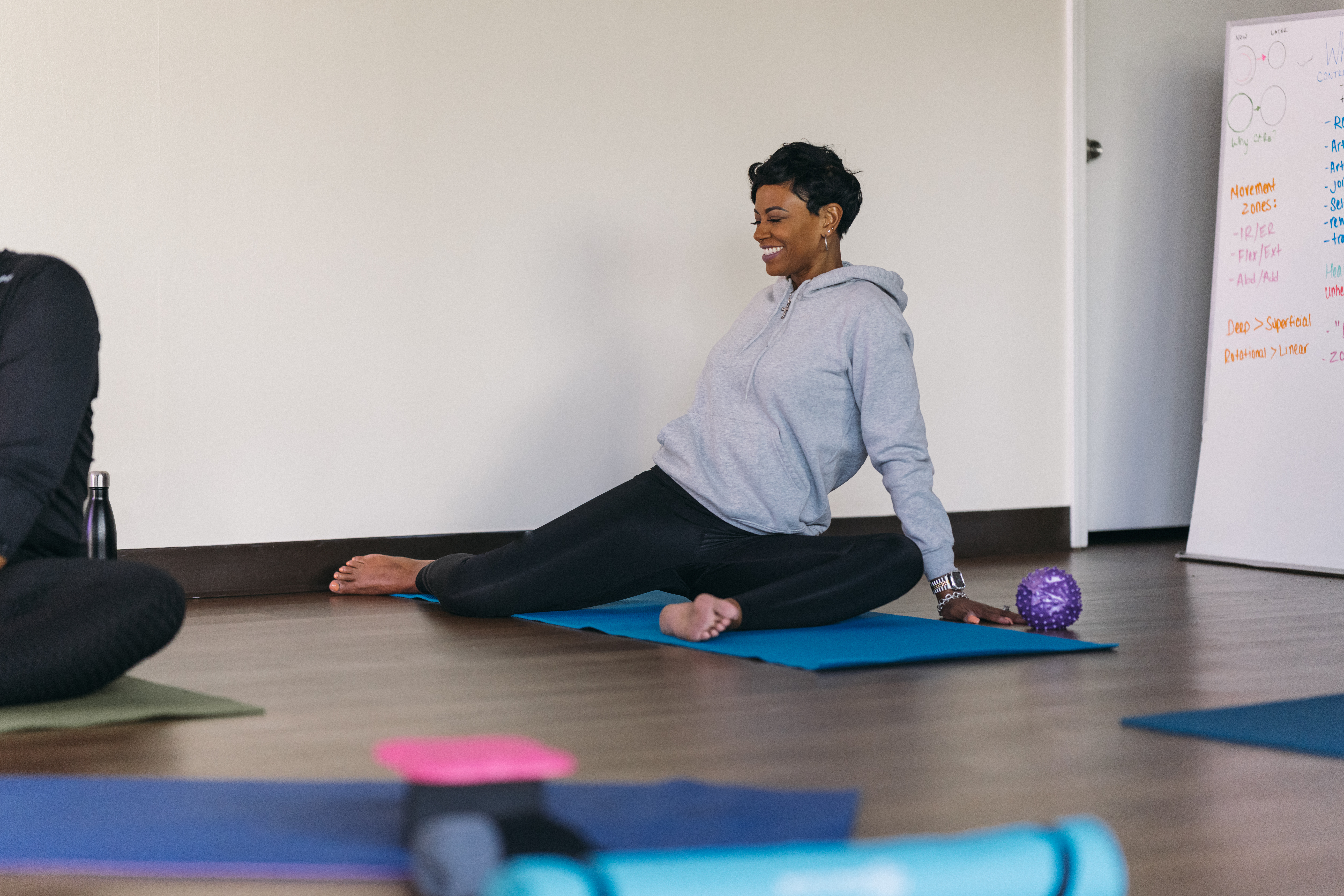 A woman performs a 90/90 hip mobility exercise, with both knees bent at 90&deg;, her left knee in front and her right knee out to the right side.
