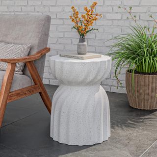 a white swirled effect contemporary outdoor side table with a book and floral arrangement on top