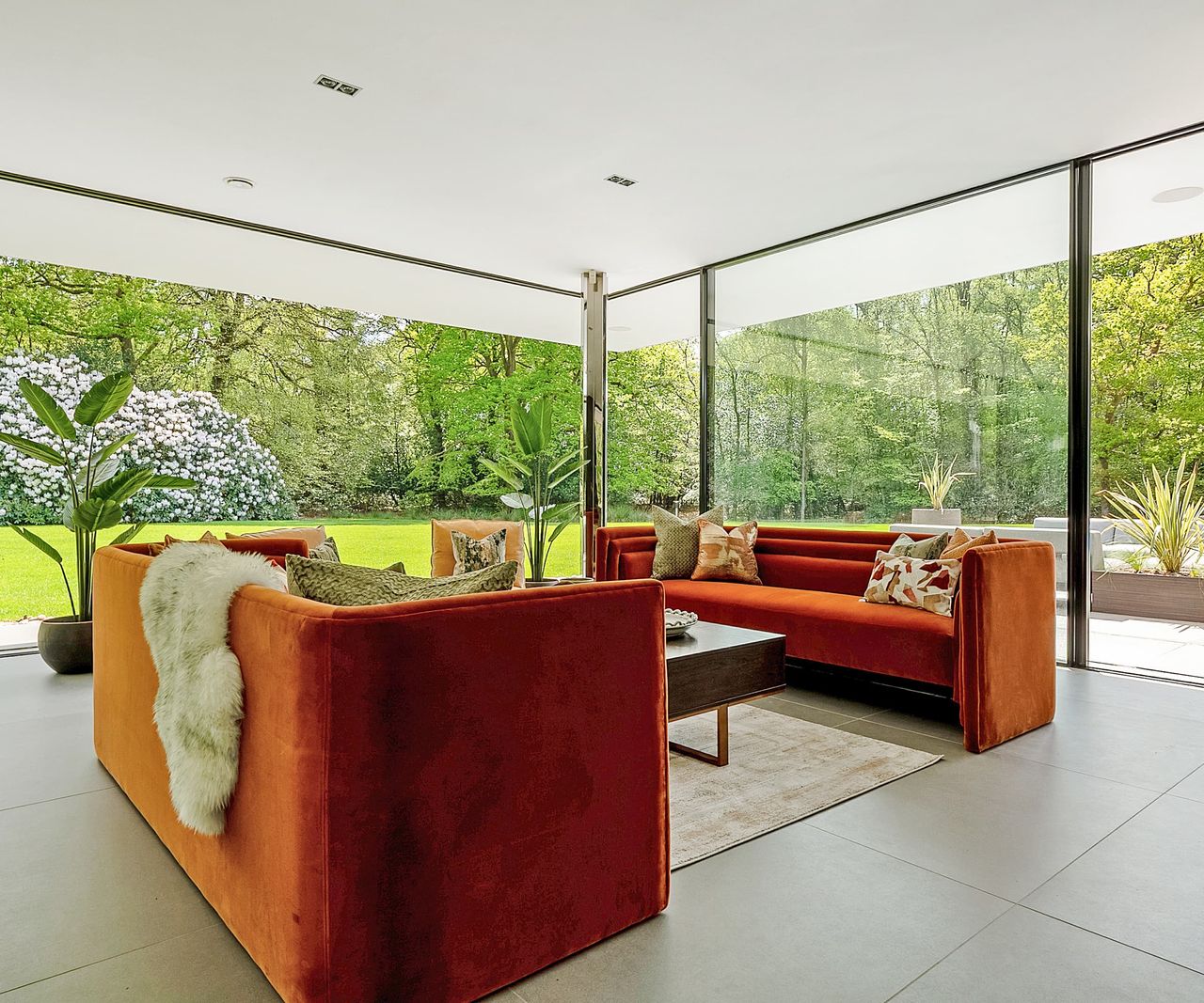 A living room with orange sofas and views of a green landscape via floor to ceiling windows