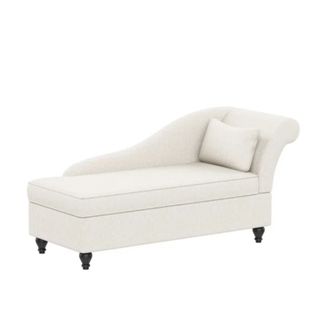 A white rectangular chaise with a curved top and white throw pillow, with three black legs at the bottom