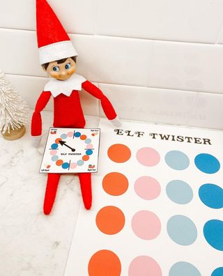 an elf with a twister board on its lap and a twister mat next to it