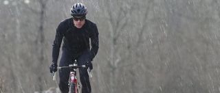 A cyclist wearing rh+ clothing cycles towards the camera in driving rain