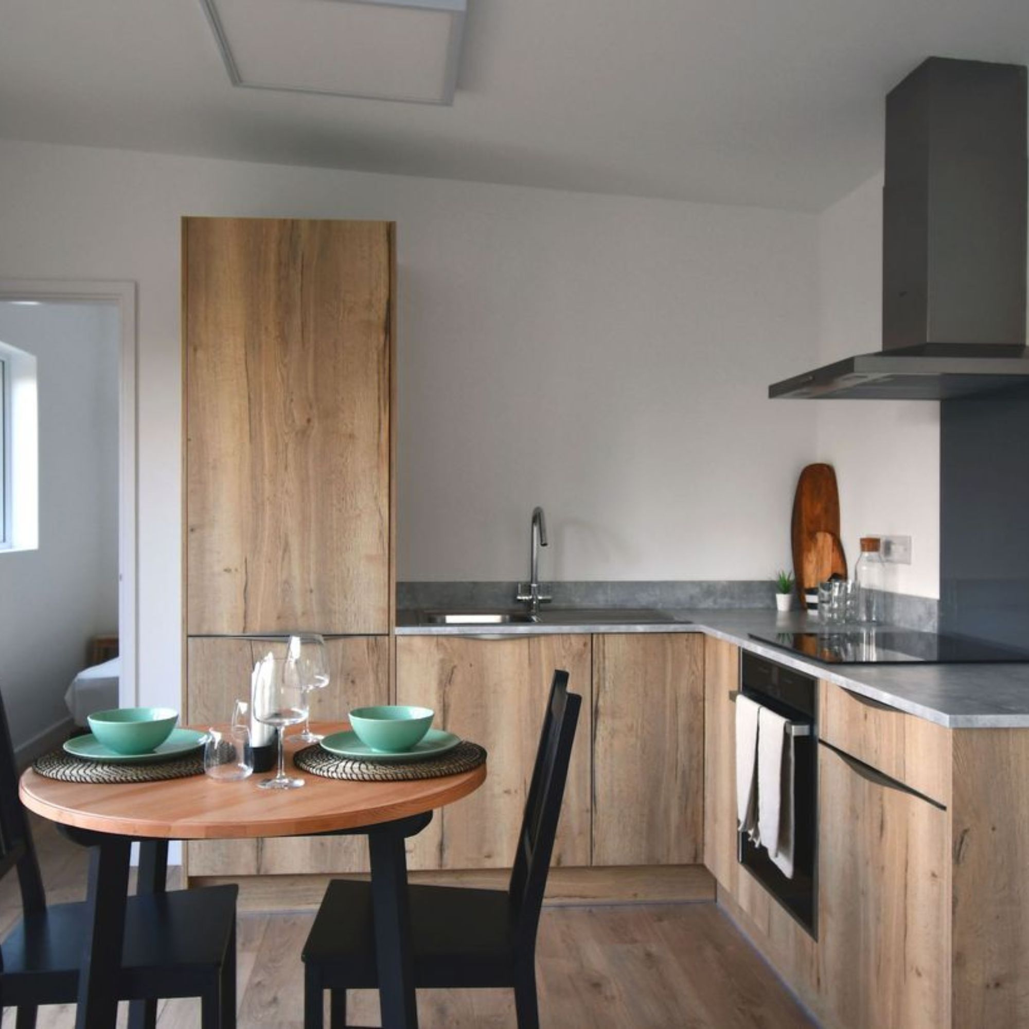 Interior of annexe with L-shaped kitchen with wood finish cabinets and circular dining table and two chairs