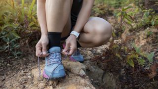 Trail runner tying shoelace wearing an Apple Watch