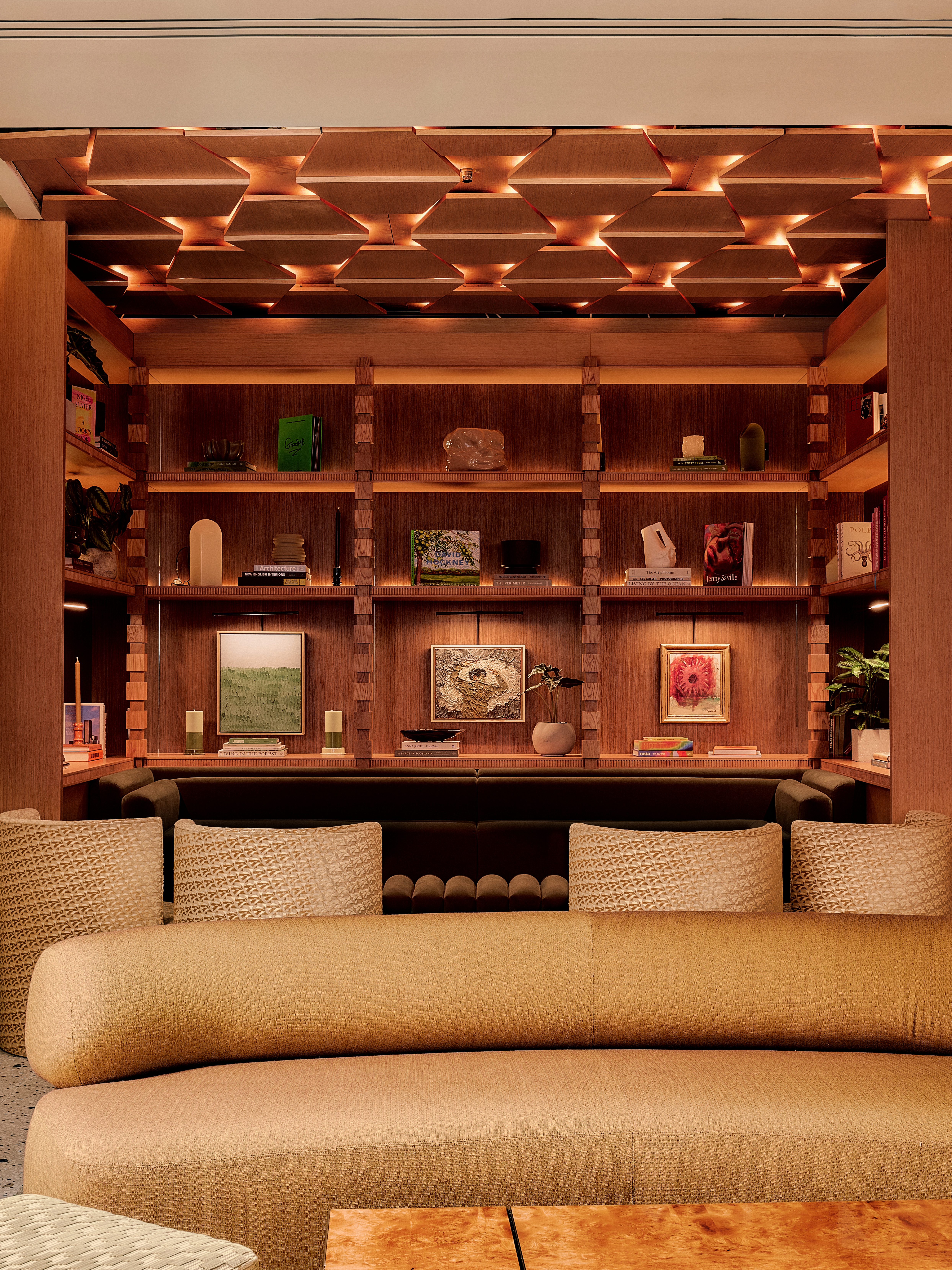 A hotel decorated with earthy hues, textural fabrics, sculptural wooden furniture with upholstered surfaces, thriving plants, abstract artworks, and warm lighting.