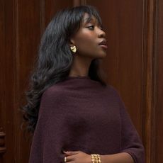 Close shot of Influencer @emmanuellek_ wearing a dark aubergine cape knit with gold earrings and a gold bracelet and ring.