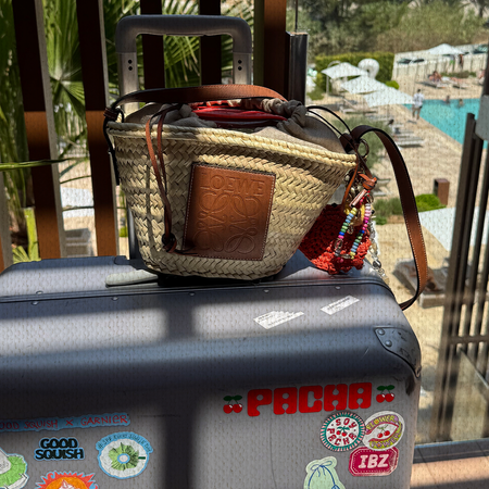 A Loewe basket bag sat on top of a suitcase covered in Ibiza-related stickers.