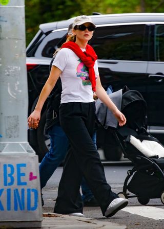 Jennifer Lawrence wearing a white tee, black pants, silver puffer shoes, and a red sweater wrapped around as a scarf while out with her family in New York City April 2024