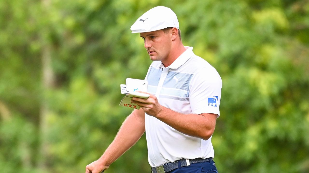 Bryson DeChambeau looks at a green reading book