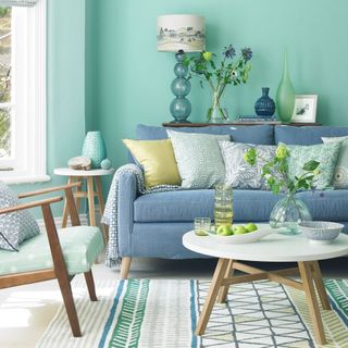 living room with blue wall blue sofa with designed cushions flower vases and lamp
