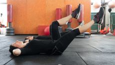 two people wearing black lying on their backs doing leg raises in the gym