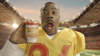 Reggie Dinkins in flashback commercial wearing football jersey and holding jar of spread in The Fall and Rise of Reggie Dinkins