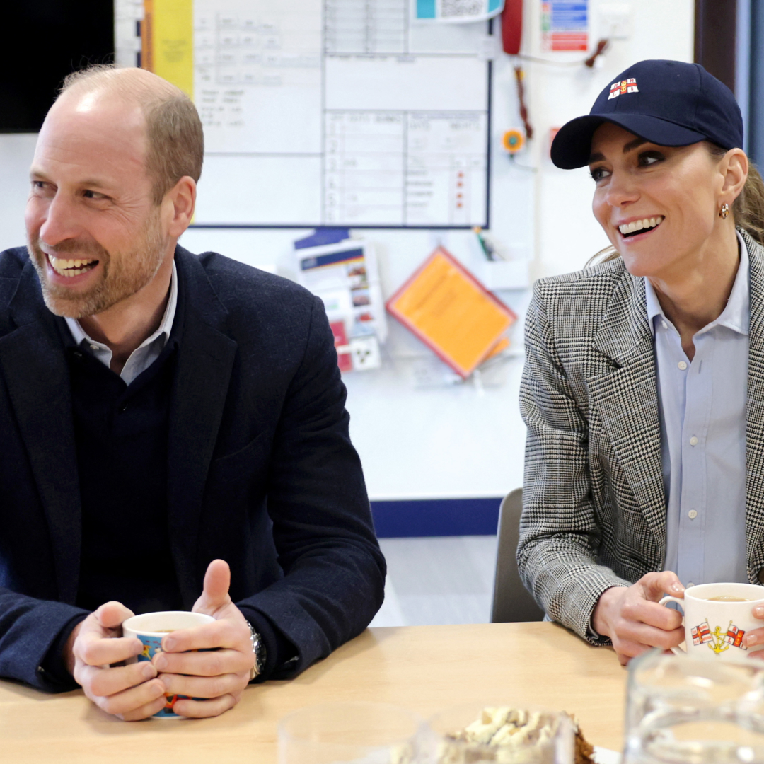 Princess Kate smiling in a baseball cap sitting next to Prince William at a table