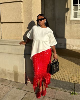 fashion influencer Nnenna Echem wearing a white T-shirt, red sequin skirt, and red mesh ballet flats