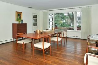 A dining room with wooden flooring and furniture, and white walls