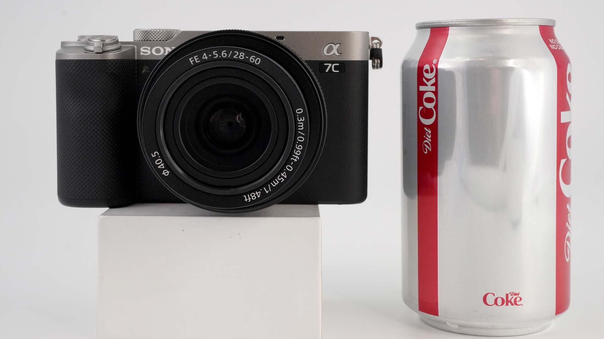 The Sony A7C on a small white pedestal next to a can of Coke. The camera is about half the height of the can