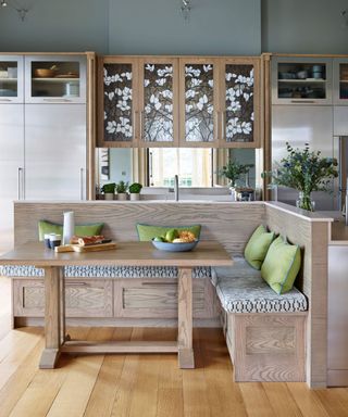 Contemporary kitchen diner with bespoke wooden banquette seating, patterned cushions, a matching wooden table, and decorative cabinets featuring floral glass inlays.