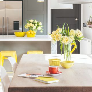 Glass vase filled with yellow flowers on top of kitchen table and countertop