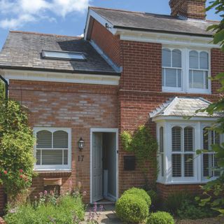 Front of a cottage house with wooden windows, a light grey front door, and a luscious front garden