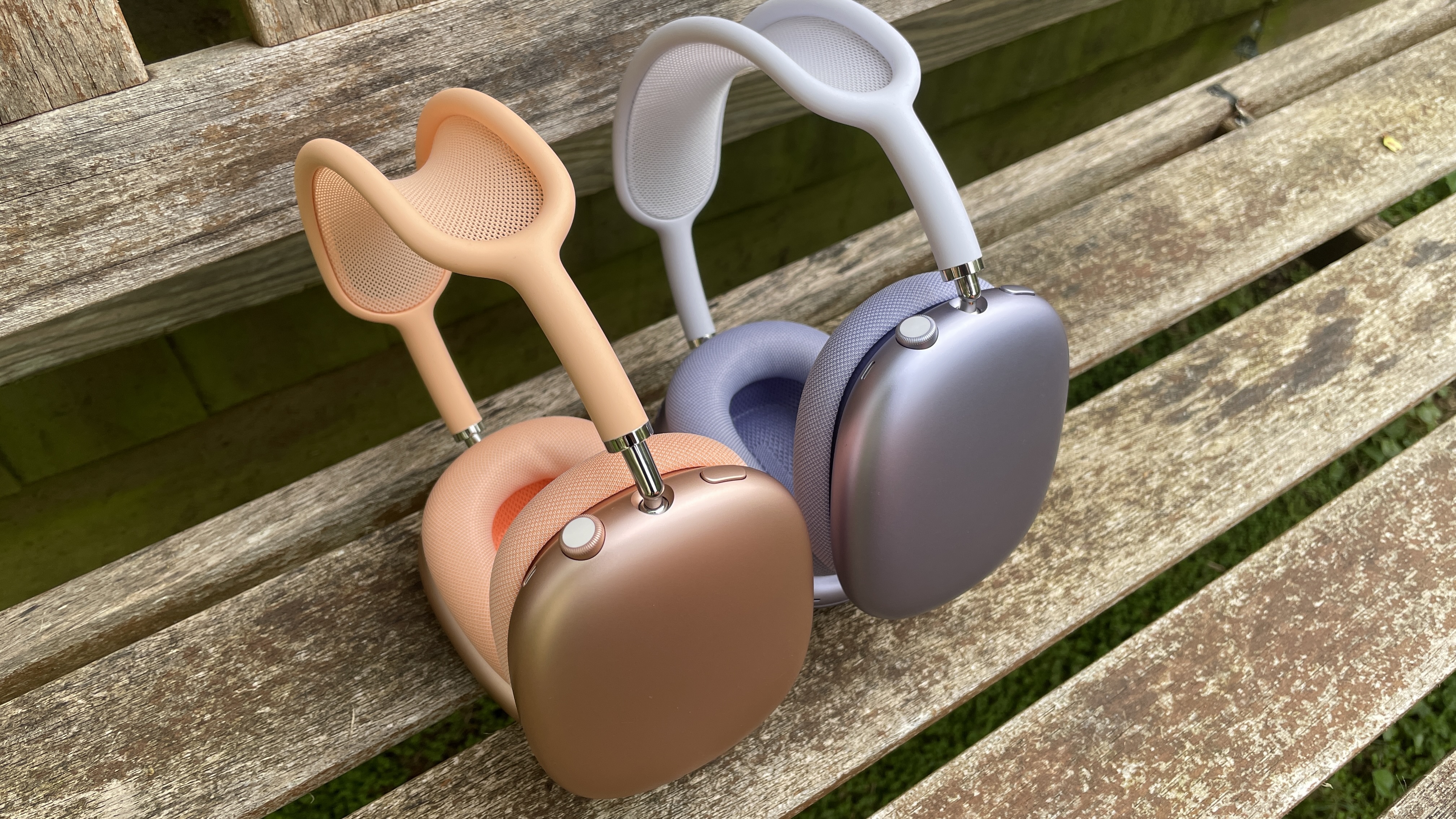 Apple AirPods Max 2 in orange with AirPods Max just visible in purple, outside in a garden on a bench, held in a hand