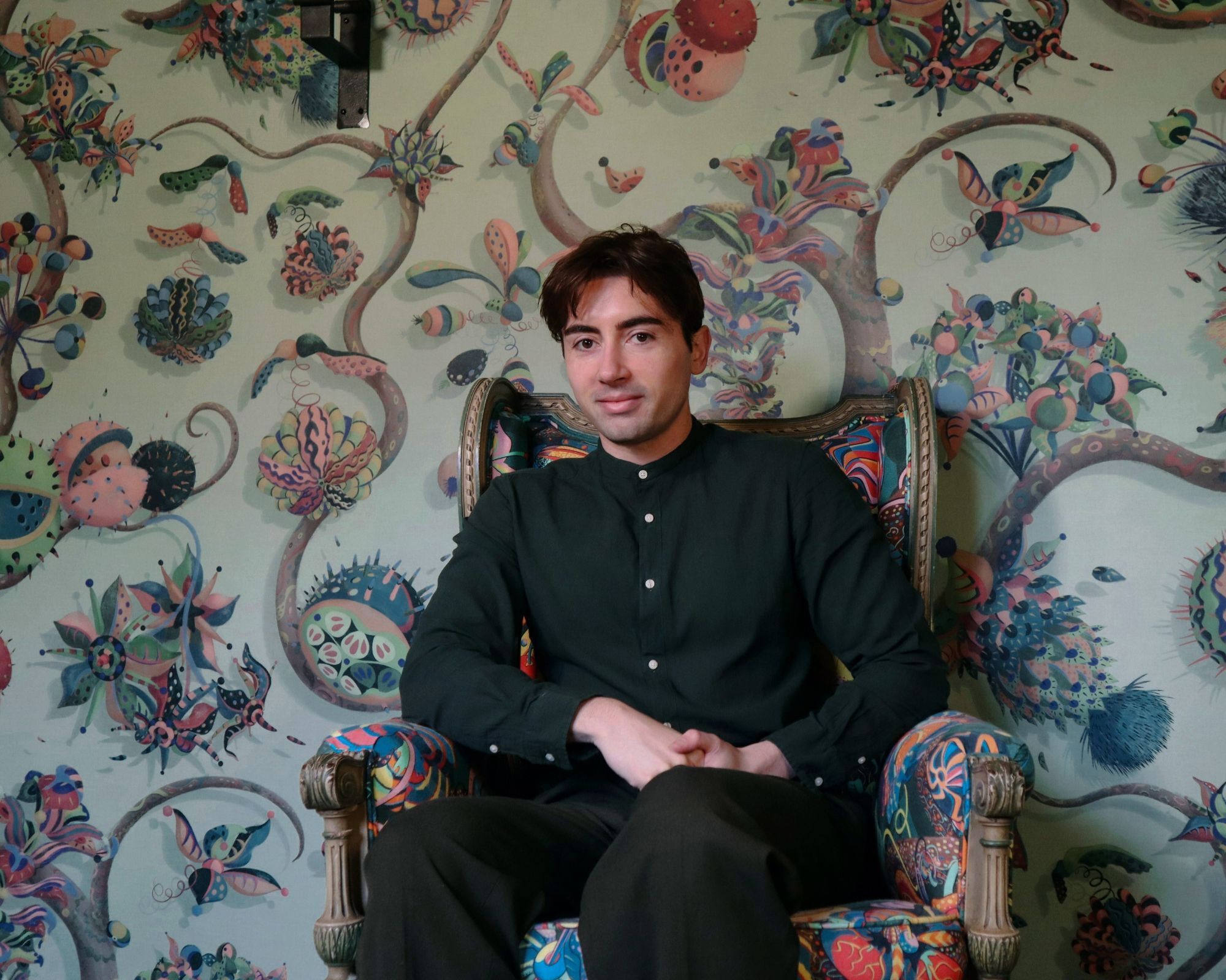 Designer Sam Wilde is sitting in front of his colourful floral wallpaper designs