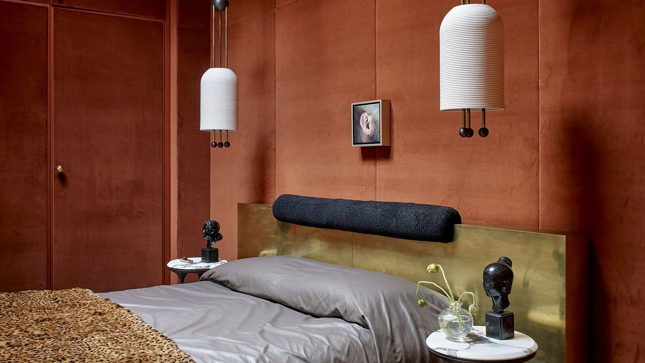 Image of a bedroom that has velvet walls in a black-orange color. The bed has a headboard is a gold material and there is a cheetah print throw pillow on the end of the bed.