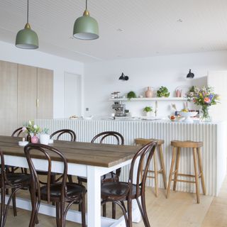 wooden dining room table and chairs on wooden flooring with green pendant lights above and white kitchen island