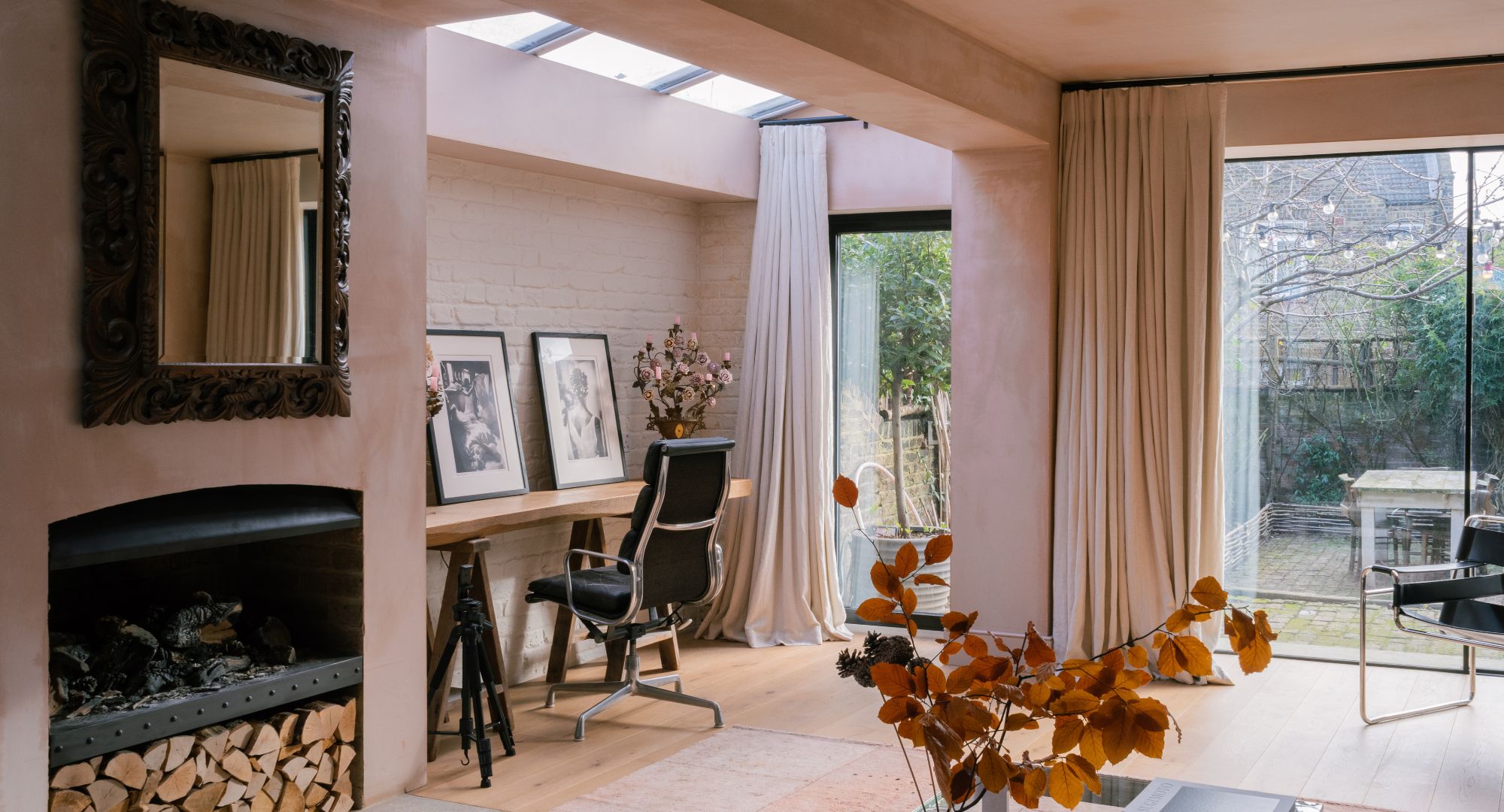 Pink plaster room with black accents including a fire place, desk chair and mirror, with two sets of curtains that pair back with the walls.