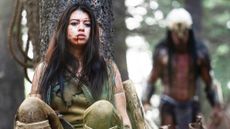 Amber Midthunder as Naru, hiding behind a tree with the Predator behind her in Prey movie on Disney Plus
