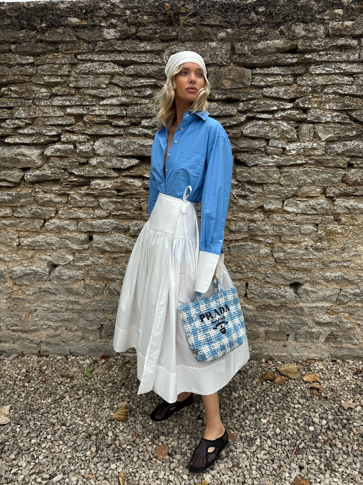 Elsa Hosk wearing a head scarf, Helsa blue button-down shirt and white poplin midi skirt, and Alaia fishnet slippers in the Cotswolds