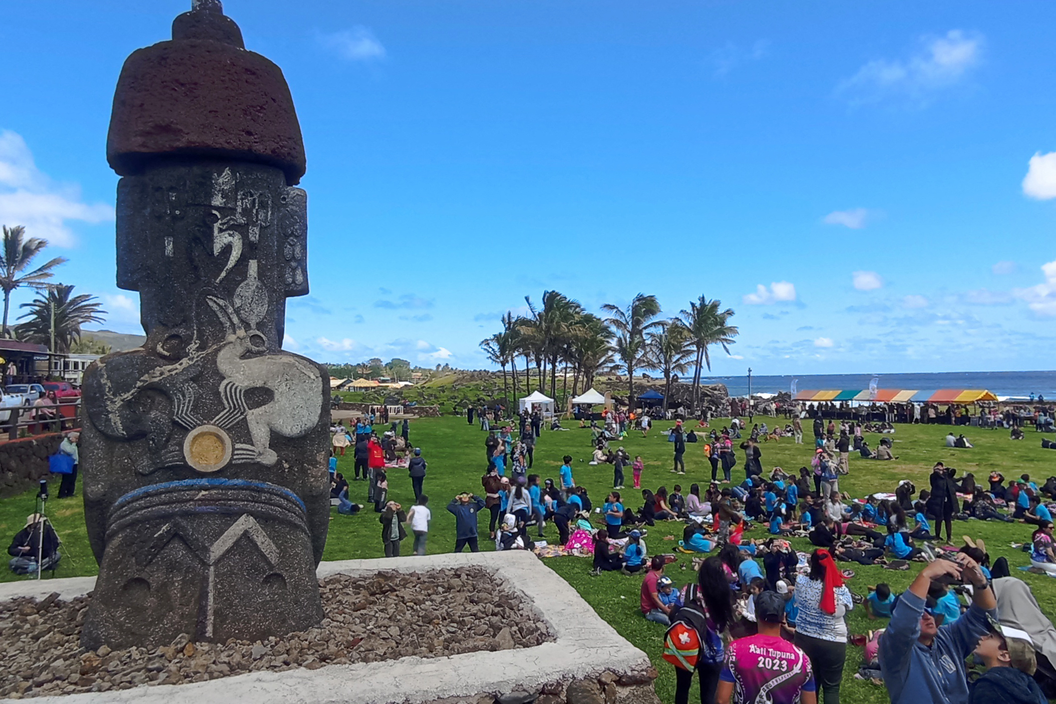 crowds gather on easter island, there is a large moai statue on the left.