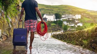 A man wheeling a suitcase and carrying red cable