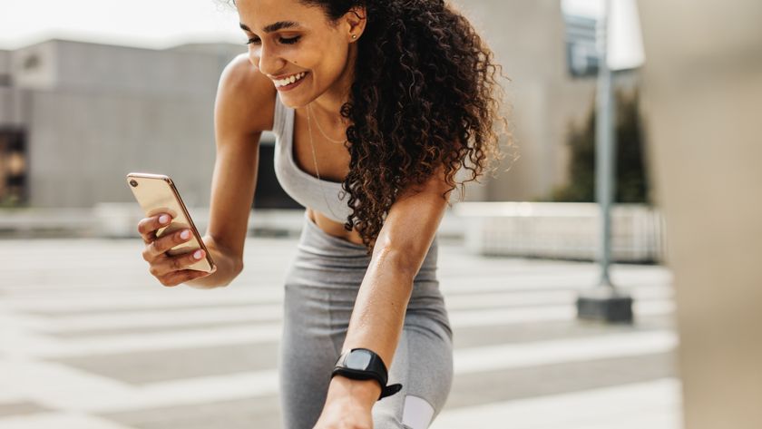 female rummer in a grey workout set smiling as she uses her phone