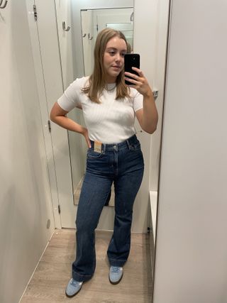 Woman in dressing room wears white t-shirt, blue jeans and blue trainers