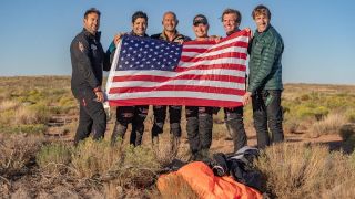 five men hold an american flag in a desert landscape.