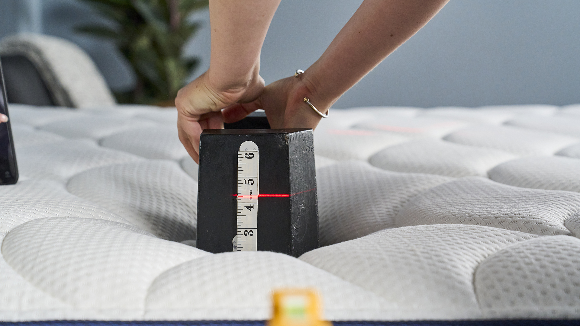 A Tom's Guide mattress tester placing a black 25kg weight on the surface of the DreamCloud Classic mattress with a red laser showing on a white measuring tape how much it is sinking